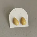 Close-up detail of glossy yellow teardrop bean stud earrings on white textured card display - Geometric Water Drop Style / Light Yellow