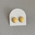 Close-up of smooth pale yellow bean-shaped stud earrings on a display card - Oval Bean Style (Style 11) / Light Yellow