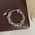 Gros plan d'un bracelet en cristal transparent avec chaîne argentée sur cuir marron. - Bracelet Modèle 17 (Cristal Haute Transparence et Étiquette Rectangulaire)