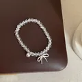 Gros plan d'un bracelet en perles de cristal blanc avec nœud et cloche en argent - Bracelet Modèle 9 (Nœud Papillon et Clochette Minimaliste)