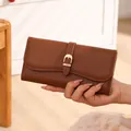 Detail view of brown pebbled leather long wallet with metal buckle closure held in hand - Brown