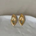 Gedetailleerde close-up van gouden geometrische holle druppeloorbellen op wit keramiek - Goud