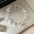Dettaglio di un bracciale di perline trasparenti con ciondolo a fiocco argentato - Stile Fiocco / Trasparente e Argento