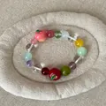 Detailopname van een kleurrijke kralenarmband met appelbedeltjes op een stoffen dienblad. - Kleurrijke Kralenstijl Met Appel