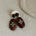 Detail view of retro dark brown wooden earrings with ornate silver cross emblem. - Style 5 Earrings