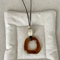 Close-up of amber geometric resin pendant necklace on beige cushion, vintage Maillard style. - Style 3 Amber Geometric Transparent Necklace