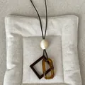Detailed close-up of a vintage amber resin geometric pendant necklace on a brown cord. - Style 4 Amber Oval Square Frame Necklace