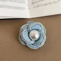 Detailed close-up of a light blue tweed camellia flower brooch with a glossy pearl center - Style 2