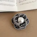 Close-up of elegant black tweed camellia brooch with central white pearl detail. - Style 4