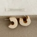 Macro view of chunky C-shaped wooden hoop earrings with natural wood grain texture - C-Hoop Studs / Beige