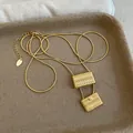 Detalle de un collar dorado con dos colgantes de bolsos trenzados sobre una bandeja. - Collar de Oro