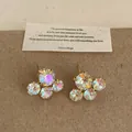 Vista detallada de pendientes de flores con cristales AB sobre un fondo de papel kraft. - Pendientes Blancos Idiscentes
