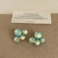 Detalle macro de pendientes de flores de cristal verde iridiscente con una tarjeta - Pendientes Verdes Idiscentes