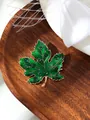 Detailed close-up of a vintage green maple leaf brooch with sparkling rhinestones on wood - Forest Green (A23-191)