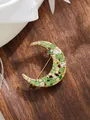 Detailed view of a golden crescent moon brooch with green and white rhinestones on wood - Crescent Moon Green and White Rhinestone (A23-155)