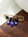 Detailed macro view of Evil Eye and Hamsa hand charms on a gold safety pin brooch. - Blue Charms Multi-Element Style (my1) / Black Bead