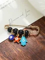 Detail view of ethnic evil eye and hamsa hand charms on a gold-toned safety pin - Blue Orange Light Blue Colorful Charms Style (my7)