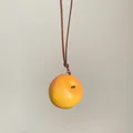 Primer plano de un colgante de manzana amarilla realista en un cordón marrón fino - Manzana Amarilla / M