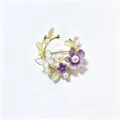 Gedetailleerde close-up van de elegante bloemenkrans broche met parels en paarse emaille bloemen. - Paars