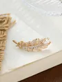 Detailansicht der eleganten goldenen Federbrosche mit glitzernden Zirkonen auf einem Buch. - Federstil (A22-106 Brosche)