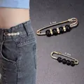 Detailansicht von zwei dekorativen Taillenverstellnadeln neben einem Modell in Jeans. - Kombination aus Schwarzer Perle & Perle (E-99) / 2 Stück/Set / Schwarz/Weiß