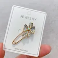 Eleganter goldener Schleifen-Broschenstift mit funkelnden Strasssteinen auf weißer Karte - Schleife 19