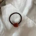 Detalle de una goma de pelo elástica marrón con una cuenta ovalada de lunares blancos. - Café