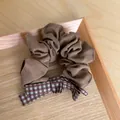 Detailed view of a brown fabric scrunchie featuring a retro plaid bow on a wooden tray - Coffee Scrunchie