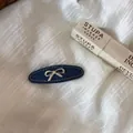Macro view of denim blue hair clip with a silver bow ornament on white fabric. - Denim Blue Duckbill Clip (2#) / Silver Bowknot Style