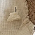 Nahaufnahme einer cremefarbenen Haarklammer aus Acetat auf einem beigen Stoffhintergrund - Haarklammer / Silberweiße Textur