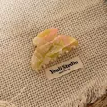 Nahaufnahme einer marmorierten Haarklammer aus Acetat in Gelb und Rosa auf Stoff - Haarklammer / Cremegelbe Textur