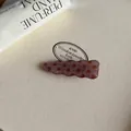 Macrobeeld van een golvende roze-bruine acetaat haarklem met een bruin vintage stippenpatroon - Roze Driehoek Golf Haarspeld