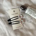 Detailansicht von zwei süßen Haarklammern im Knopf-Stil mit Blumenmustern auf Karte. - Weiß Bunte Sternknopf-Stil / 2er-Pack / Weiß Bunte Sternknopf Schwarze Haarklammer