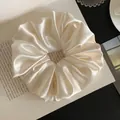 Elegant cream satin scrunchie with ruffled texture displayed on an open book. - L / White