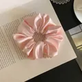 Close-up detail view of a soft pink satin scrunchie placed on an open vintage book - S / Pink