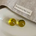 Detailansicht der gelben transparenten Harz-Ohrstecker auf minimalistischem Leinenstoff - Gelb