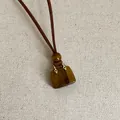 Detailaufnahme eines Tigerauge-Handtaschenanhängers an einer braunen Kordelkette. - Tigerauge Taschen-Halskette