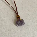 Detailaufnahme eines lilafarbenen Naturstein-Handtaschenanhängers an brauner Kordel - Amethyst Tasche Halskette
