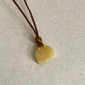 Detailopname van een handtasvormige gele natuurstenen hanger aan een bruine koordketting - Topaas Tas Ketting