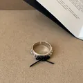 Primo piano di un anello aperto d'argento con motivo a pianeti e un fiocco di corda nera - Anello con Fiocco Placcato Oro