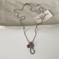 Detailopname van een zilveren kralenketting met een getextureerde schijf en rode paddenstoel. - Ketting