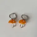 Makro-Detail von handgefertigten orangefarbenen Pilz-Ohrringen aus Glas auf Weiß. - Creolen-Stil / Orange