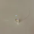 Macro view of an iridescent cube pendant on a transparent fishing line necklace cord. - Crystal Sugar Cube Necklace