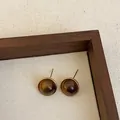 Detail shot of round brown resin stud earrings with gold bezel in a wooden tray. - Style 2 (925 Silver Post)