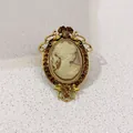 Close-up detail of a vintage Victorian cameo brooch with amber rhinestones and gold frame. - Hollow Scroll Pattern Border / Light Brown Cameo Style (A12-107)