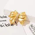 Dettaglio macro di una spilla vintage a fiocco dorato con eleganti decorazioni in perle lucide - Oro (J-107)