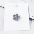 Eleganter blumenförmiger Kristall-Brosche-Pin mit irisierendem Zentrum auf weißem Karton - Blumenstil / Silber