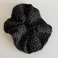 Close-up of elegant black scrunchie with white floral patterns and crinkled pleated texture - Black Floral Scrunchie
