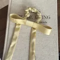 Detailopname van een champagne satijnen scrunchie met lange linten op een getextureerd boek. - Strik Haarelastiekje / Geel