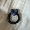 Primer plano detallado de un coletero con corazón de cuadros azules sobre tela texturizada - Lazo para el Pelo de Corazón a Rayas Azul y Negro